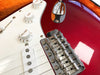 Close-up of red electric guitar body showing white pickguard, chrome bridge with "Fender" engraving, volume and tone control knobs, and pickups.