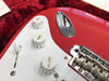 Close-up of red electric guitar control knobs with tone and volume settings, white pickguard, and chrome bridge hardware on plush red case lining
