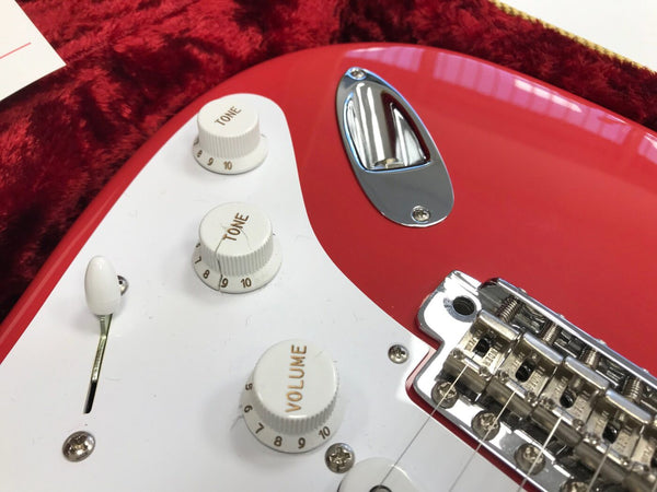 Close-up of red electric guitar control knobs with tone and volume settings, white pickguard, and chrome bridge hardware on plush red case lining