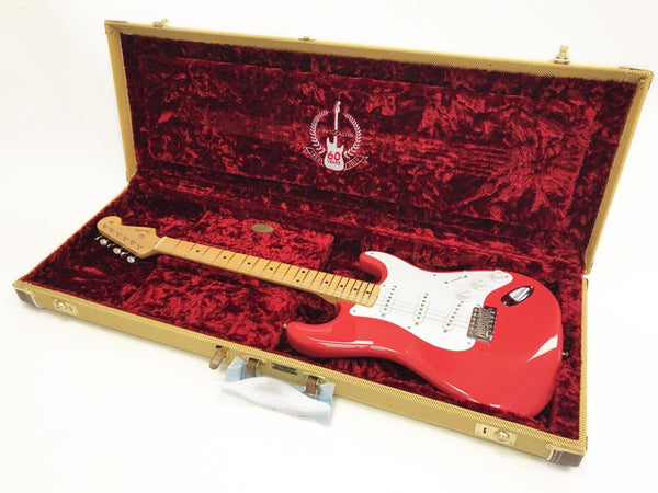 Red Fender Stratocaster electric guitar with maple neck in open tweed hard case lined with red plush interior, 60th anniversary edition emblem visible inside case