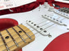 Close-up view of red electric guitar with white pickguard, maple fretboard, and single-coil pickups in hard case with red plush lining