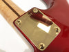 Close-up of red electric guitar neck plate with serial number P56911 and four gold screws on a natural wood neck