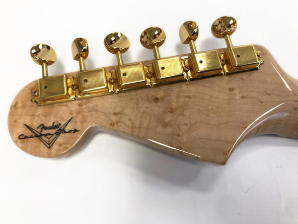 Close-up of Fender Custom Shop guitar headstock with birdseye maple wood and gold tuning pegs on white background