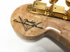Close-up of Fender Custom Shop guitar headstock with natural wood finish and gold tuning pegs showing detailed logo and wood grain texture