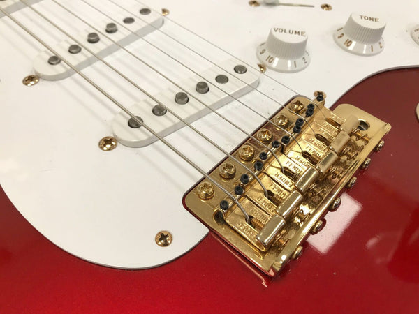 Close-up of red electric guitar with white pickguard, gold bridge, white volume and tone knobs, and single-coil pickups