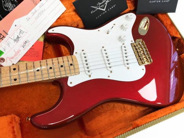 Fender Stratocaster electric guitar in candy apple red finish with white pickguard, maple neck, gold hardware, and custom care tags in an orange plush guitar case