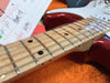 Close-up of maple guitar neck with metal frets and strings on a red electric guitar body with paperwork in the background