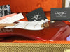 Close-up of red Fender Stratocaster electric guitar inside tweed hard case with Fender Custom Shop documentation and care booklets on orange plush lining