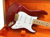Red electric guitar with white pickguard and gold hardware in orange plush guitar case