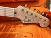 Close-up of Fender Stratocaster guitar headstock with gold tuning pegs and maple neck in orange plush guitar case