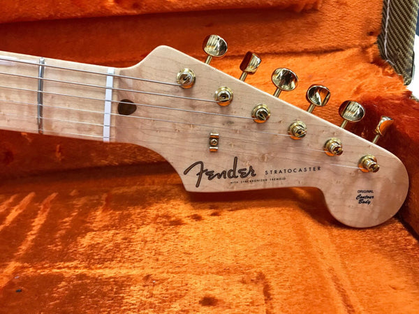 Close-up of Fender Stratocaster guitar headstock with gold tuning pegs and maple neck in orange plush guitar case