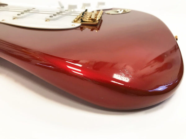 Close-up of glossy red electric guitar body with gold hardware and white pickguard on white background