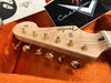 Close-up of Fender Stratocaster guitar headstock with gold tuning pegs inside orange plush guitar case with Fender Custom Shop paperwork