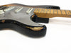 Close-up of black electric guitar body with silver pickguard and worn finish showing wood underneath, maple neck with fretboard and dot inlays on white background