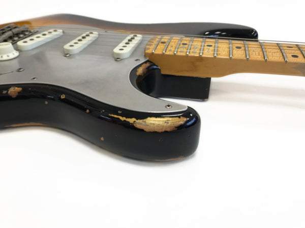 Close-up of black electric guitar body with silver pickguard and worn finish showing wood underneath, maple neck with fretboard and dot inlays on white background