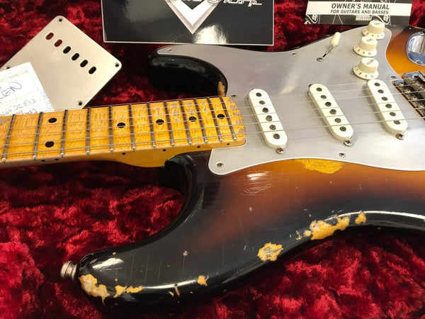 Close-up of vintage sunburst electric guitar with maple neck and worn finish on red velvet background, showing white pickups and control knobs with owner's manual and guitar parts.