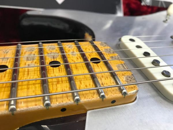 Close-up of worn maple guitar fretboard with metal frets and steel strings on electric guitar neck near single-coil pickups