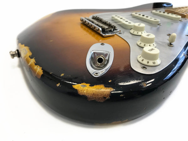 Close-up of sunburst electric guitar body with worn and chipped finish showing relic wear, featuring white tone knobs and output jack socket.