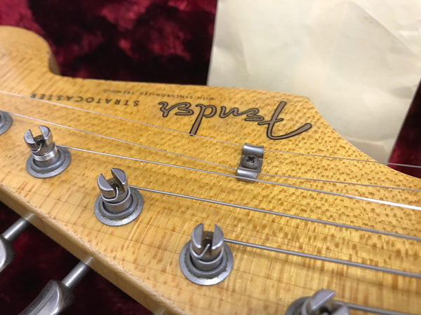 Close-up of vintage Fender Stratocaster guitar headstock with worn wood finish and tuning pegs, showcasing Fender logo and string tree hardware.
