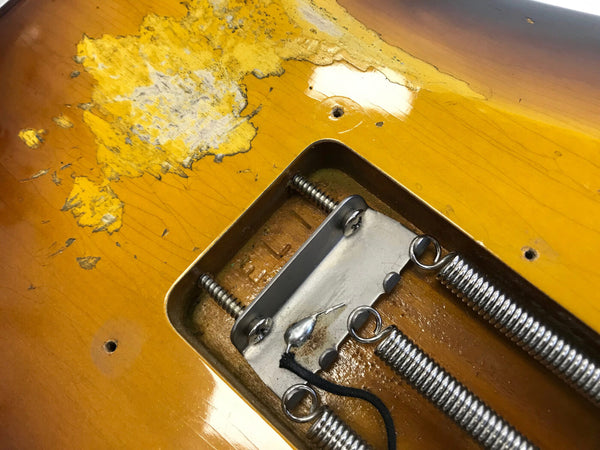 Close-up of vintage electric guitar body with worn yellow finish and exposed metal springs in tremolo cavity
