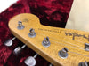Close-up of Fender Stratocaster guitar headstock with vintage tuning pegs on a red plush guitar case lining