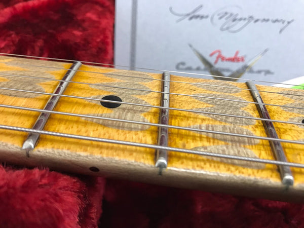 Close-up of maple guitar neck with black dot inlay and metal frets on six strings, resting on red plush case lining and blurred Fender certificate in background