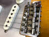 Close-up of Fender guitar bridge and strings showing vintage metal saddle design and white single-coil pickups on a light wood body electric guitar