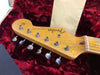 Close-up of vintage Fender Stratocaster guitar headstock with tuning pegs in red plush-lined case