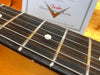 Close-up of Fender guitar rosewood fretboard with metal frets and white dot inlays against an orange background