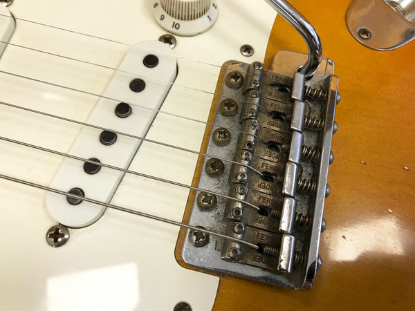 Close-up of vintage Fender electric guitar bridge and white single-coil pickup with six strings and tone control knob