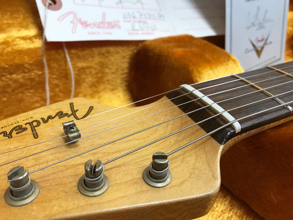 Close-up detail of Fender guitar headstock with tuning pegs and strings on orange velvet background