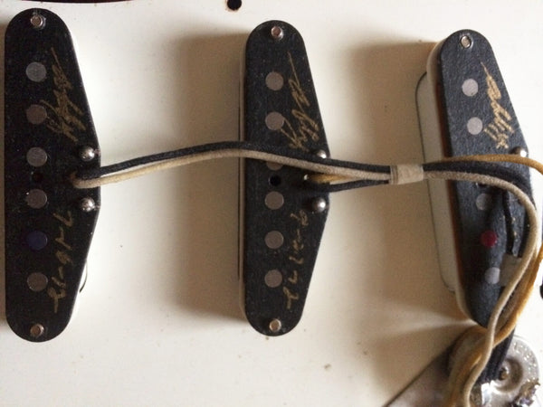 Close-up of vintage Fender Stratocaster single-coil pickups with cloth-covered wiring and handwritten markings on pickup covers.