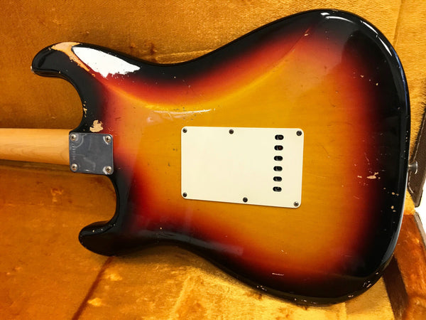 Vintage sunburst electric guitar body with worn finish and white backplate, displayed in an orange velvet-lined guitar case.