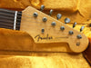 Close-up of Fender Stratocaster electric guitar headstock with tuning pegs and original contour body logo, resting on a yellow plush guitar case lining.