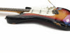 Close-up of vintage sunburst electric guitar body with white pickguard and tremolo arm showing worn paint and chips on black edge