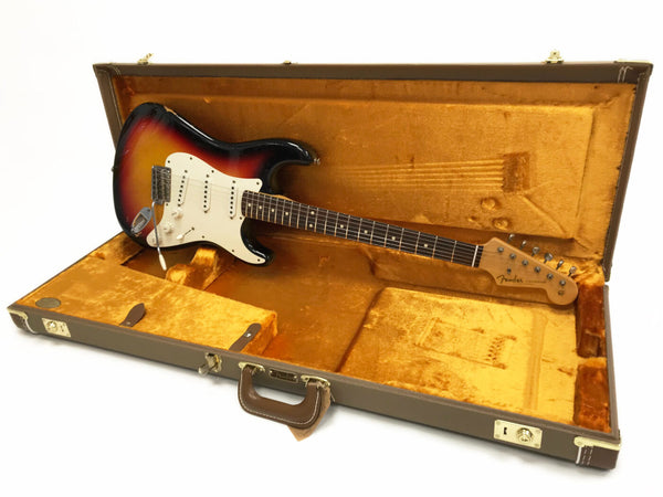 Fender Stratocaster electric guitar in sunburst finish resting in vintage brown hard shell guitar case with orange plush interior lining