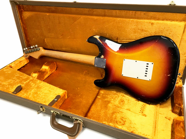 Vintage sunburst electric guitar with maple neck resting in open orange velvet lined hard case, back view