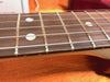 Close-up image of guitar fretboard with metal frets, dot inlays, and steel strings on a wooden neck against an orange background