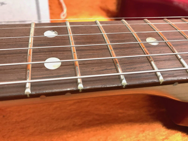 Close-up image of guitar fretboard with metal frets, dot inlays, and steel strings on a wooden neck against an orange background