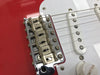 Close-up of Fender electric guitar bridge and white single-coil pickup on red body with volume knob visible