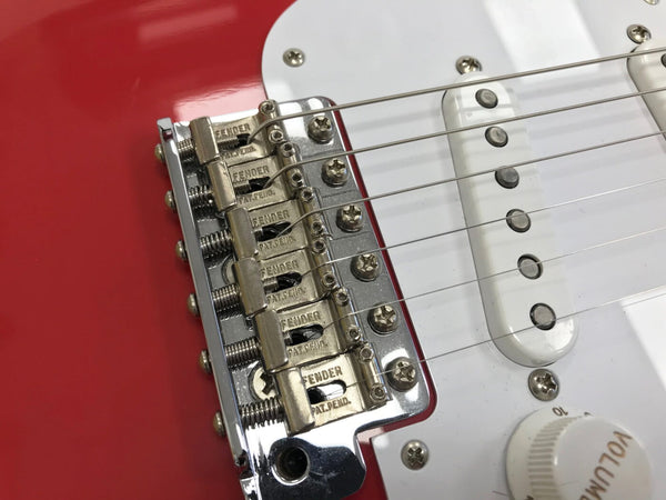 Close-up of Fender electric guitar bridge and white single-coil pickup on red body with volume knob visible