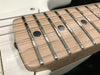 Close-up of maple guitar neck with dot inlays and metal frets on white electric guitar body