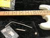 Close-up of white electric guitar neck and body with maple fretboard, showing tremolo arm, spring, and guitar case interior accessories from Coffee House Guitars product listing.