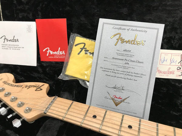 Fender Stratocaster guitar headstock with tuning pegs, Fender Certificate of Authenticity for Stratocaster Pro Closet Classic, Fender owner's registration, warranty booklet, and yellow Fender polishing cloth in black guitar case.
