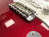 Close-up of chrome bridge and saddles on red electric guitar body with white pickguard and volume knob.