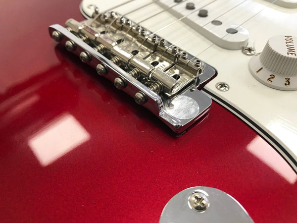 Close-up of chrome bridge and saddles on red electric guitar body with white pickguard and volume knob.