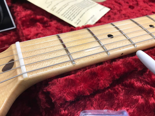 Close-up of maple guitar neck and fretboard with metal frets and strings on red plush case lining at Coffee House Guitars.