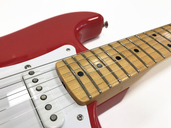 Close-up of red electric guitar with maple fretboard and white single-coil pickups showing metal strings and fret markers