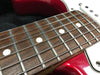 Close-up of electric guitar fretboard with rosewood fingerboard, metal frets, white dot inlays, and red glossy body near the neck pocket