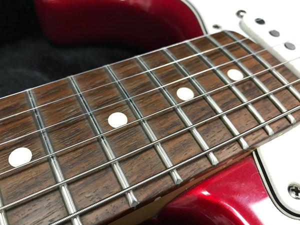 Close-up of electric guitar fretboard with rosewood fingerboard, metal frets, white dot inlays, and red glossy body near the neck pocket